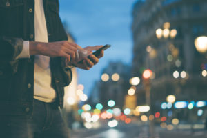 Closeup image of male hands with smartphone at night on city street, searching internet or social networks, hipster man typing an sms message on chat